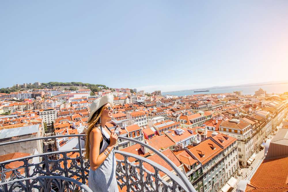 Young woman tourist enjoying beautiful cityscape top view on the old town during the sunny day in Lisbon city, Portugal during all-inclusive wellness holiday