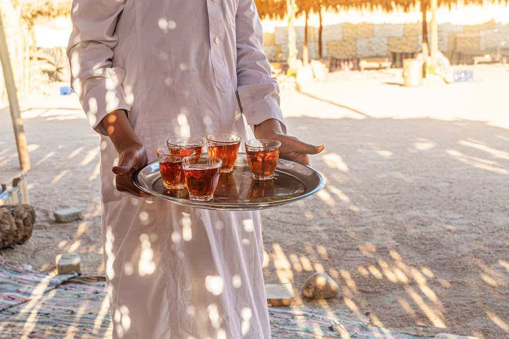 A tray with mugs of traditional Egyptian tea in the waiter's hand. Bedouin welcome a cup of tea with almonds, Sinai.